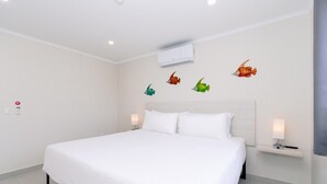 Een hotelkamer met een groot bed, witte beddengoed, een hoofdbord, bedlampen en een wandairconditioner.