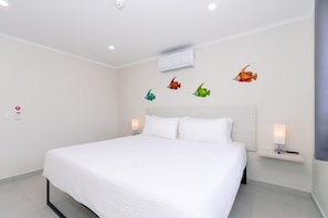 A hotel room with a large bed, white bedding, a headboard, bedside lamps, and wall-mounted air conditioning unit. - Aruba Escape! 2BR Condo w Shared Pool Near Beaches (Noord)