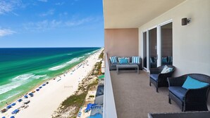 A balcony with wicker furniture and a view of a beach with umbrellas and people. - REFRESHED CONDO! READY FOR YOU! 3/2 GULF FRONT! SLEEPS 10! (Panama City Beach)