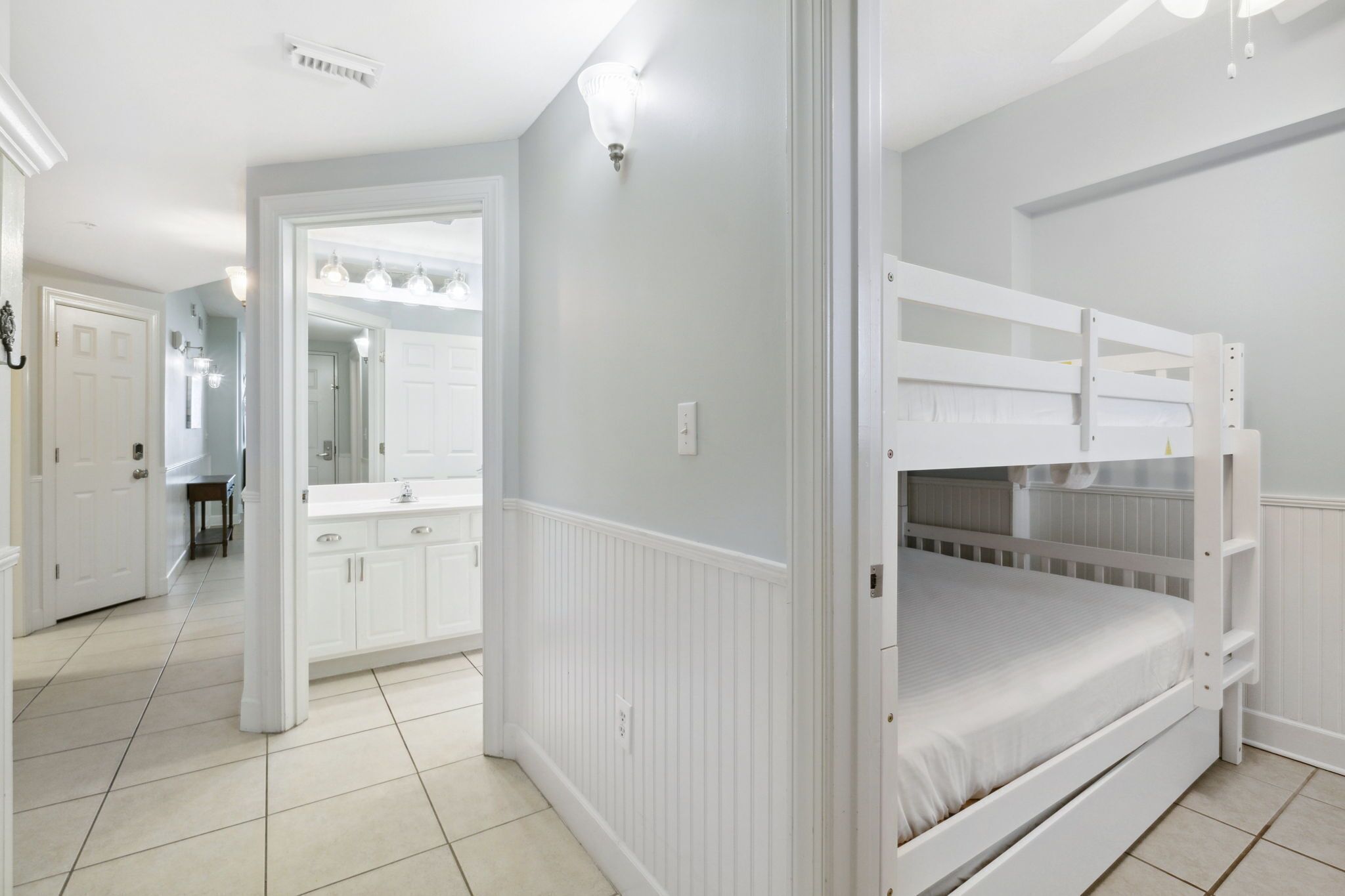 Une chambre avec un lit superposé, une salle de bain avec un meuble-lavabo et un couloir menant à une autre pièce.