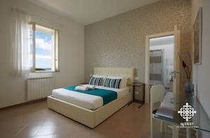 A bedroom with a bed, a bedside table, a chair, a window with curtains, and a patterned wall.