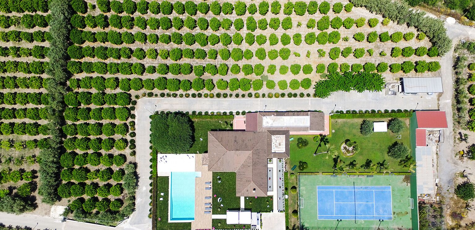 Luftaufnahme eines Anwesens mit Swimmingpool, Tennisplatz und angelegten Gartenbereichen.