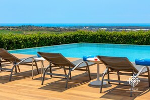 A poolside area with lounge chairs and a table, overlooking a scenic landscape with a view of the sea. - Sicily Summer Breeze (Ispica)
