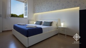 Un dormitorio moderno con una cama grande, una ventana con cortinas, un radiador y una mesita de noche con lámpara.