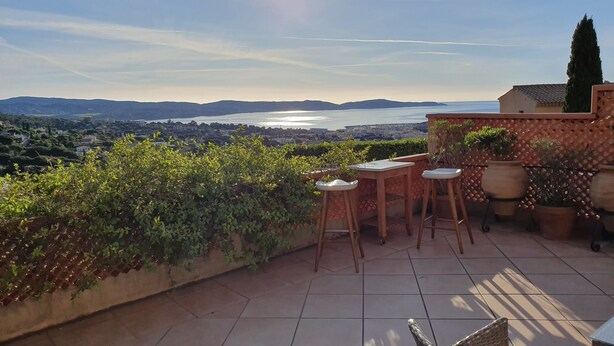 A terrace with a view of a body of water, surrounded by greenery and potted plants.