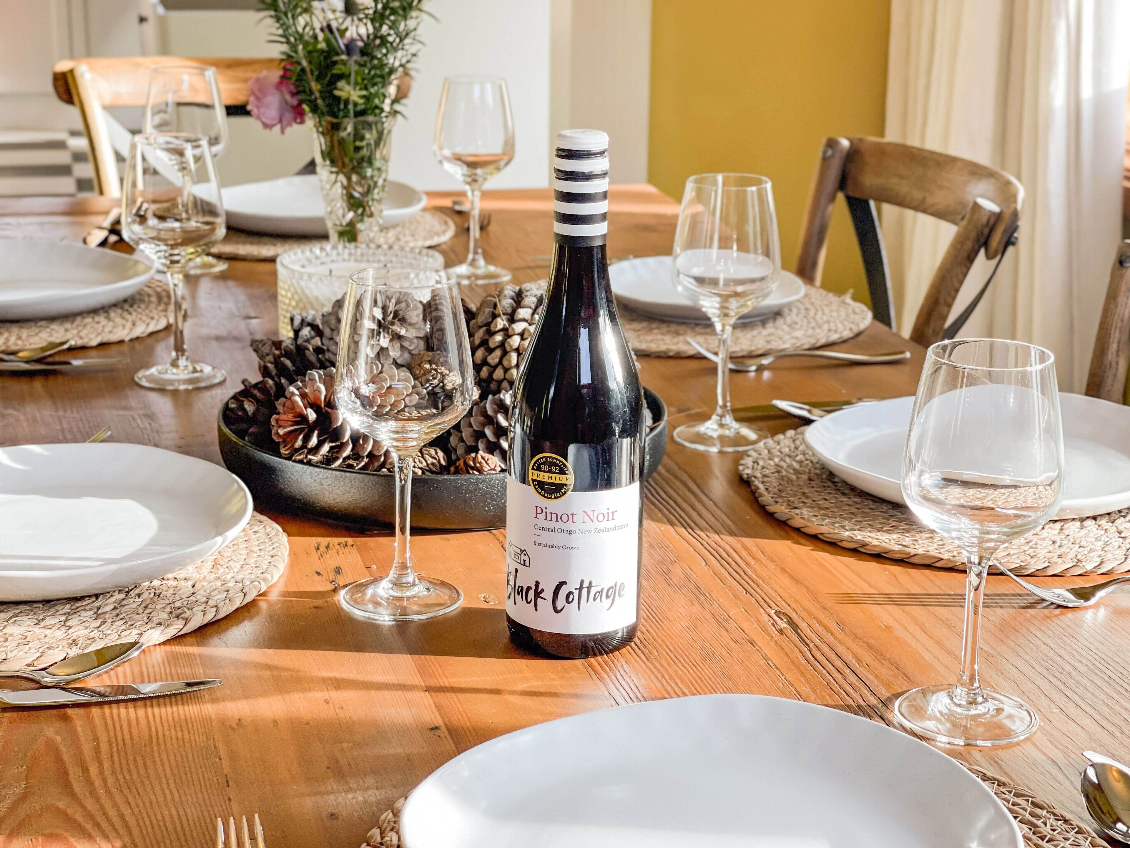 A dining table set with plates, cutlery, and wine glasses, with a bottle of Pinot Noir prominently displayed.