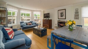 A living room with a sofa, a coffee table, a dining table with chairs, a fireplace, and a bookshelf. - Spacious  5 bedroom split level flat with three bathrooms and open plan kitchen living area, sleeps (Seaview)
