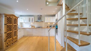 A modern kitchen with white cabinets, a wooden floor, and a staircase with wooden steps and white railings. - Spacious  5 bedroom split level flat with three bathrooms and open plan kitchen living area, sleeps (Seaview)