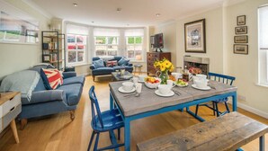 A modern living room with a dining area, featuring a large window, a fireplace, and a collection of framed pictures on the wall. - Spacious  5 bedroom split level flat with three bathrooms and open plan kitchen living area, sleeps (Seaview)