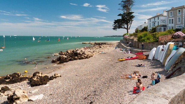A pebble beach with boats, a tree, and a building with a sign. - Spacious  5 bedroom split level flat with three bathrooms and open plan kitchen living area, sleeps (Seaview)