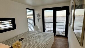 Une chambre à coucher comprenant un lit, une fenêtre, une porte donnant sur un balcon et un luminaire fixé au mur.