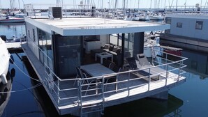 Une terrasse flottante comprenant un espace repas, des sièges extérieurs et une vue sur le port de plaisance.