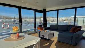 A modern living room with a sofa, a dining table, and a view of a marina. - Hausboot in Boltenhagen (Boltenhagen)