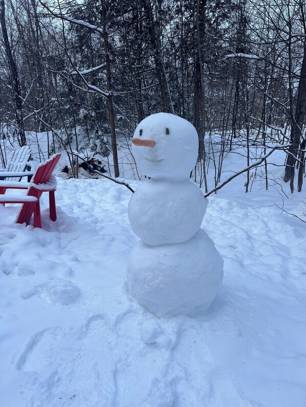 A snowman in a snowy outdoor setting with a red chair nearby. - Secluded Lakeside Cottage in Beautiful Whitestone (Whitestone)