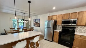 A modern kitchen with a central island, stainless steel appliances, wooden cabinets, and a dining area with chairs. - Secluded Lakeside Cottage in Beautiful Whitestone (Whitestone)
