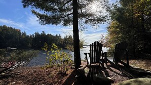 A lakeside deck with Adirondack chairs, a dock, and a forested backdrop. - Secluded Lakeside Cottage in Beautiful Whitestone (Whitestone)