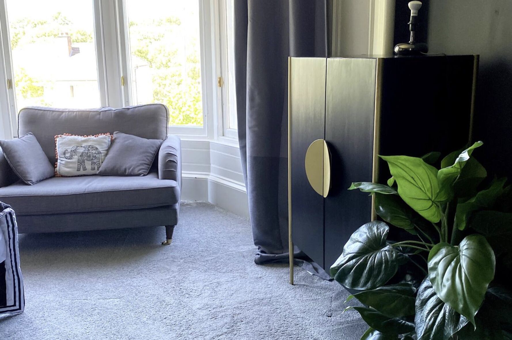 Un salon avec un canapé gris, un meuble sombre et une grande plante verte.
