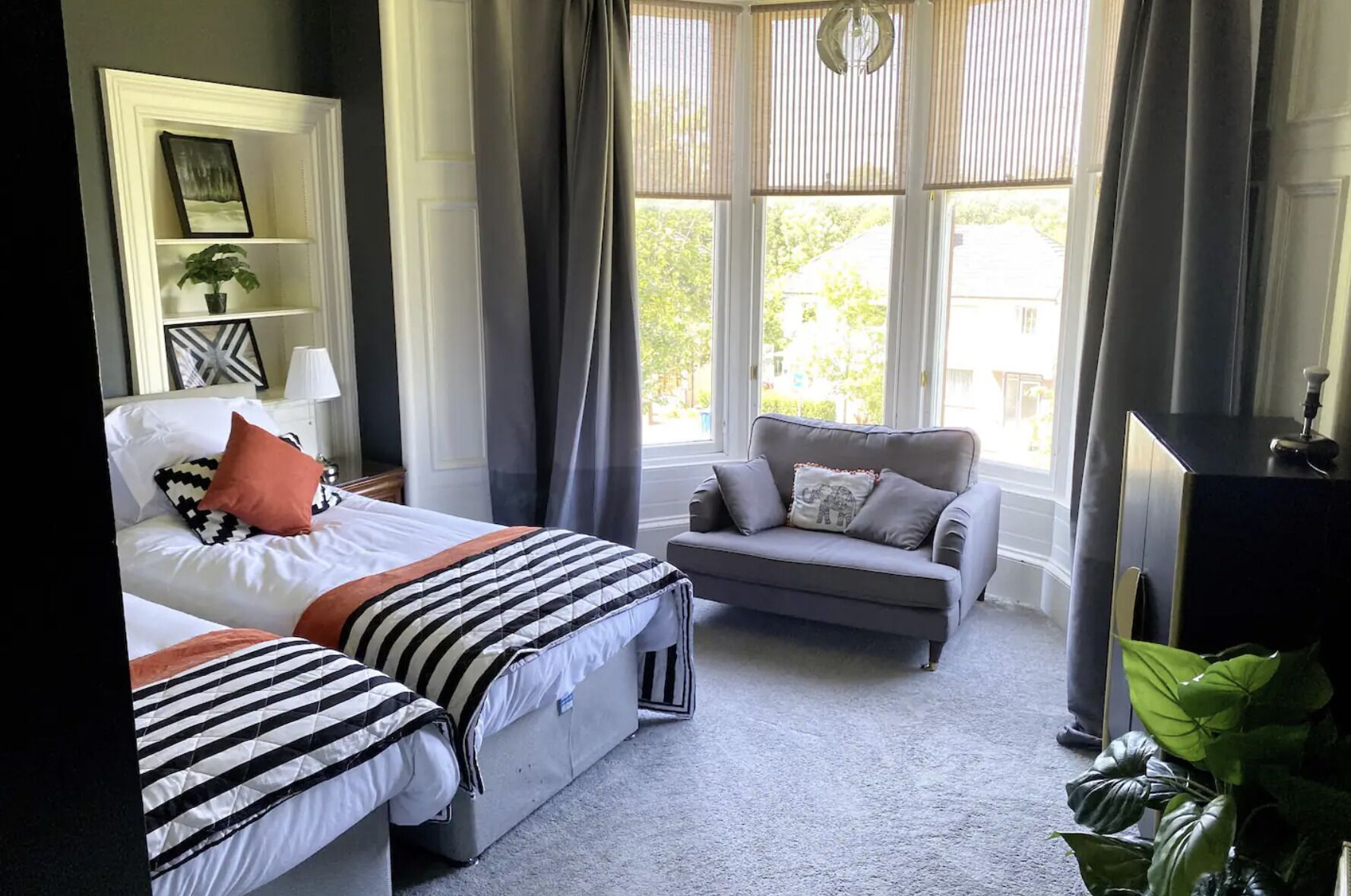 A bedroom with a bed, two bedside tables, a grey sofa, a TV, and a window with curtains.