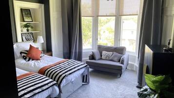 A bedroom with a bed, two bedside tables, a grey sofa, a TV, and a window with curtains.