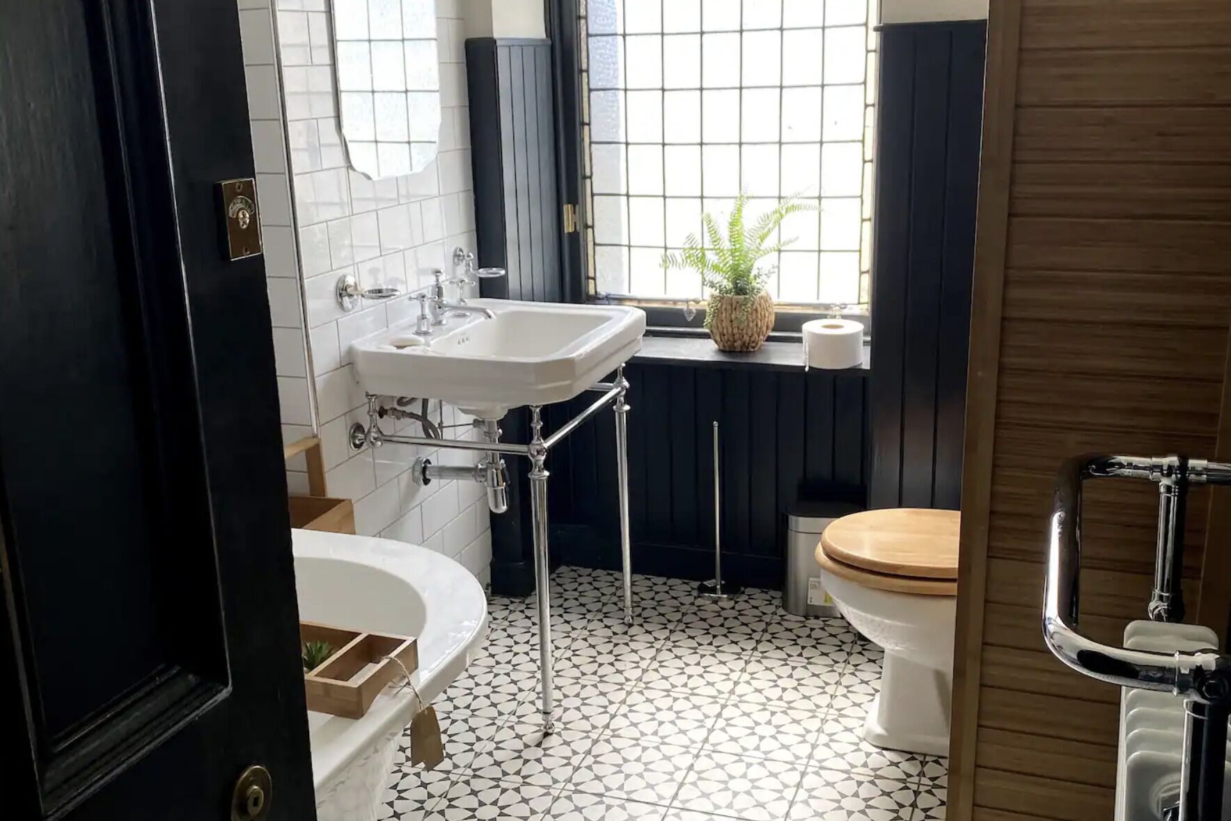 A bathroom with a white sink, a bathtub, a toilet, and a window with a plant.