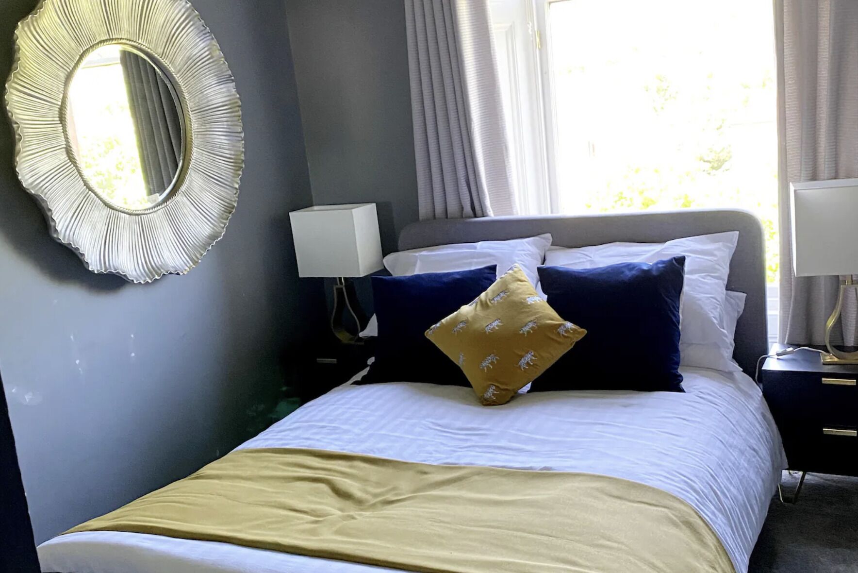 A neatly made bed with a white and yellow bedspread, a blue headboard, and a decorative mirror on the wall.