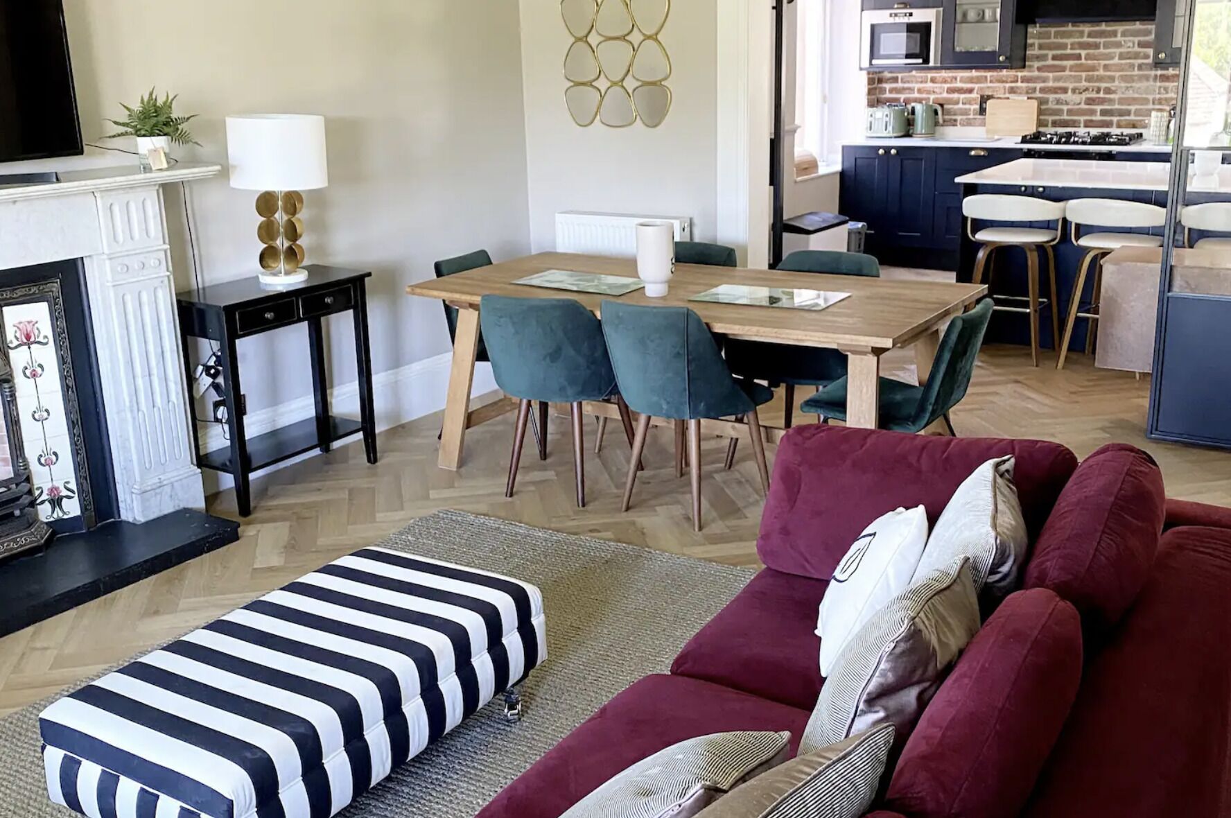 A modern living room with a striped ottoman, a red sofa, and a dining area with a wooden table and chairs.