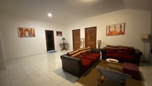 A spacious living room with a sofa set, a coffee table, and a lamp. There are doors leading to other rooms and a painting on the wall. - Résidences Gamly (Mamoudzou)