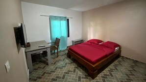 A hotel room with a bed, a desk, a chair, a television, and a window with curtains. - Résidences Gamly (Mamoudzou)