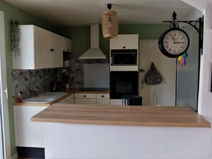Una cocina con armarios blancos, encimera de madera, microondas, horno y un reloj colgante.