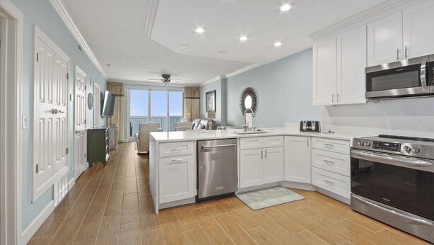 A modern kitchen with white cabinets, stainless steel appliances, and a view to the outside. - Emerald Isle 2110 - Front row beach chair service included! Affordable rates (Panama City Beach)