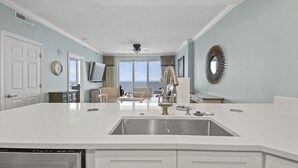 A modern kitchen with a large island, a dining area with a view, and a living space with a ceiling fan. - Emerald Isle 2110 - Front row beach chair service included! Affordable rates (Panama City Beach)