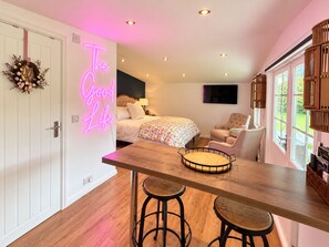 Una habitación con una cama, un escritorio con taburetes, un letrero de neón y vistas al exterior.