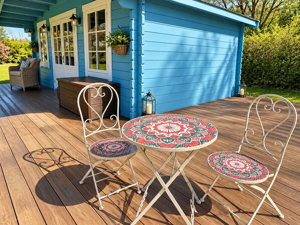 Une terrasse en bois avec un bâtiment bleu, une table ronde entourée de chaises et un banc.