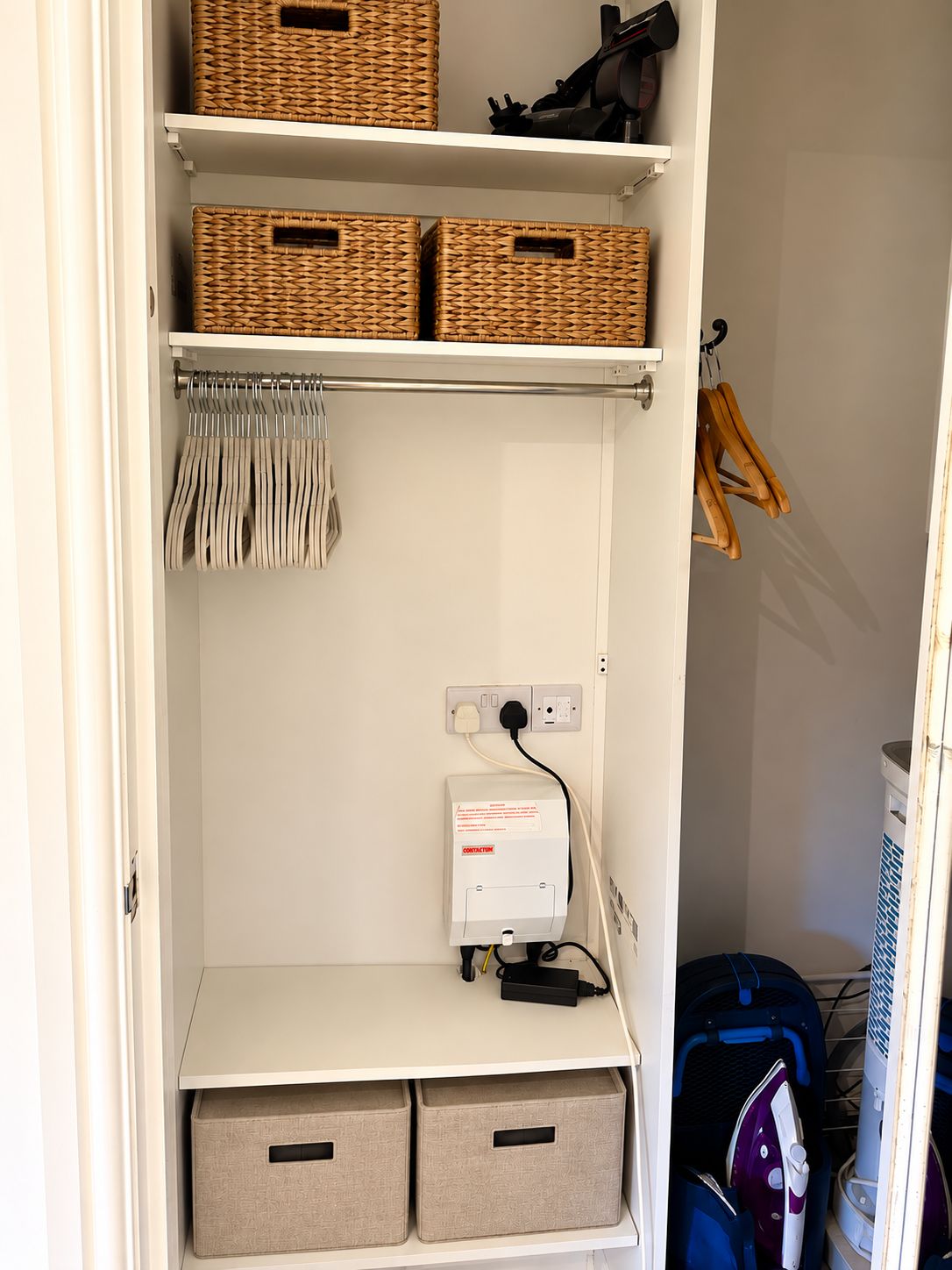 A closet with shelves, baskets, hanging clothes, and a power outlet.