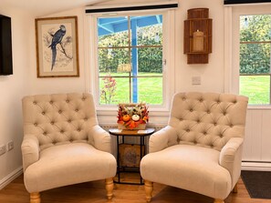 A room with two upholstered armchairs, a framed artwork, a window with a view of greenery, and a small table with a decorative arrangement. - Cosy Countryside Lodge, 10 Mins From the Beach and National Park (Maybole)