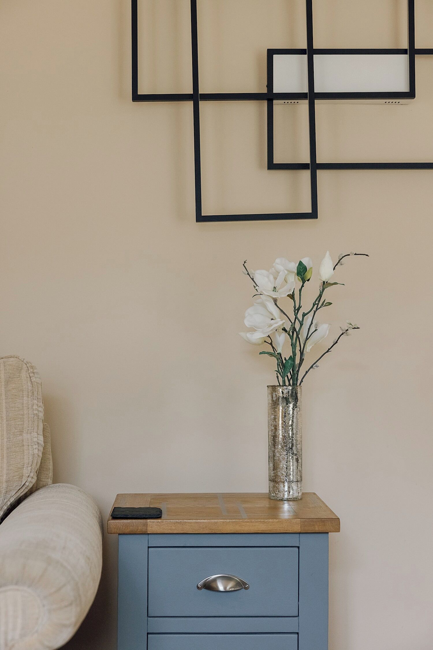 A bedside table with a vase of flowers, a drawer, and a wall with geometric art.