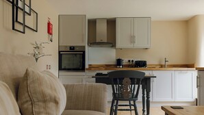 Ein Wohnzimmer mit einer Couch, einem Holztisch und einer Küche im Hintergrund.