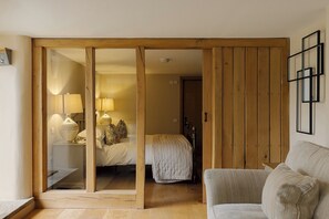 A room with a bed, a bedside table with lamps, a wooden wardrobe, and a sofa. - Dunsa Cottage, Bakewell | Peak District (Bakewell)