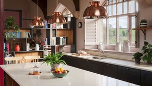 A kitchen with a white countertop, copper pendant lights, a window with a view of the countryside, and a bookshelf filled with books and decorative items. - Wesleyan, Bolton Abbey Estate (Barden)