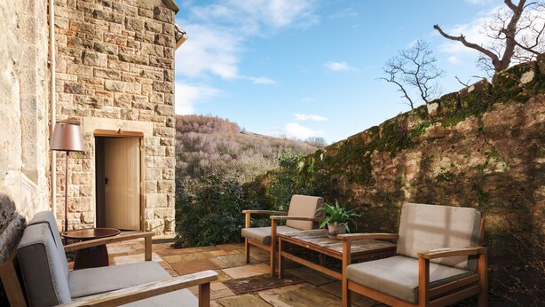 A stone building with a wooden table and two chairs, a lamp, and a potted plant. - Wesleyan, Bolton Abbey Estate (Barden)