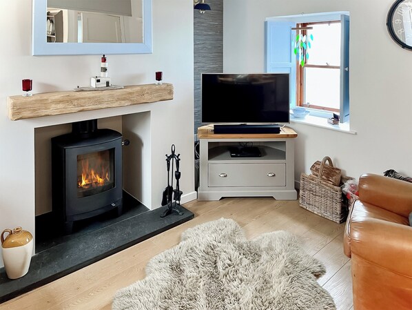 Una sala de estar acogedora con chimenea, un televisor sobre un mueble de madera, una cesta de mimbre y un sofá de cuero.