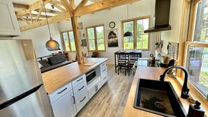 Une cuisine moderne avec des poutres en bois, un réfrigérateur en acier inoxydable, un plan de travail en bois et une fenêtre donnant sur un jardin.