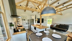 Une cuisine moderne avec des poutres en bois, un grand îlot central et un coin repas avec une table dressée pour quatre personnes.