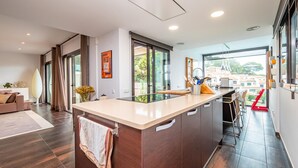 A modern kitchen with a large island, sliding glass doors to a balcony, and a view of the city.
