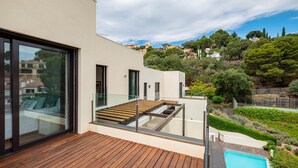 A modern house with a wooden deck, a glass-enclosed balcony, and a swimming pool.