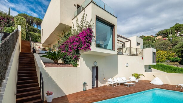 A modern house with a wooden deck, a swimming pool, and a staircase leading to a balcony.