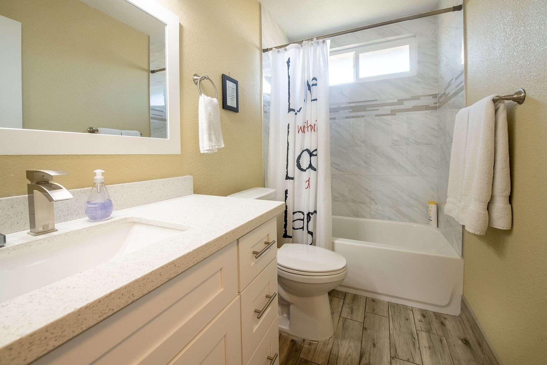 Une salle de bain avec un lavabo blanc, des toilettes et une baignoire. Il y a un rideau de douche avec du texte imprimé dessus.