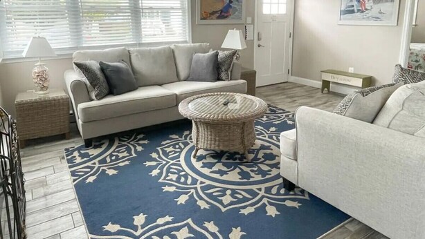 A living room with a sofa, a round wicker coffee table, a patterned rug, and artwork on the walls. - 231 33rd St Unit A  2BR Beach Home Hideaway  Parking (Brigantine)