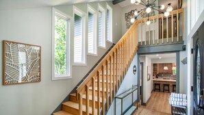 Eine Treppe mit Holzwangen führt zu einer zweiten Etage, ein Essbereich mit Bar und eine Küche sind durch eine offene Tür sichtbar.