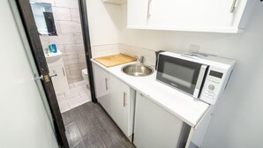 Eine kleine Küche mit Mikrowelle, Spüle und Schneidebrett aus Holz.